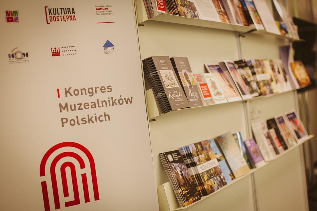 Stoisko promocyjne z folderami muzeów. Logotyp I Kongresu Muzealników Polskich 