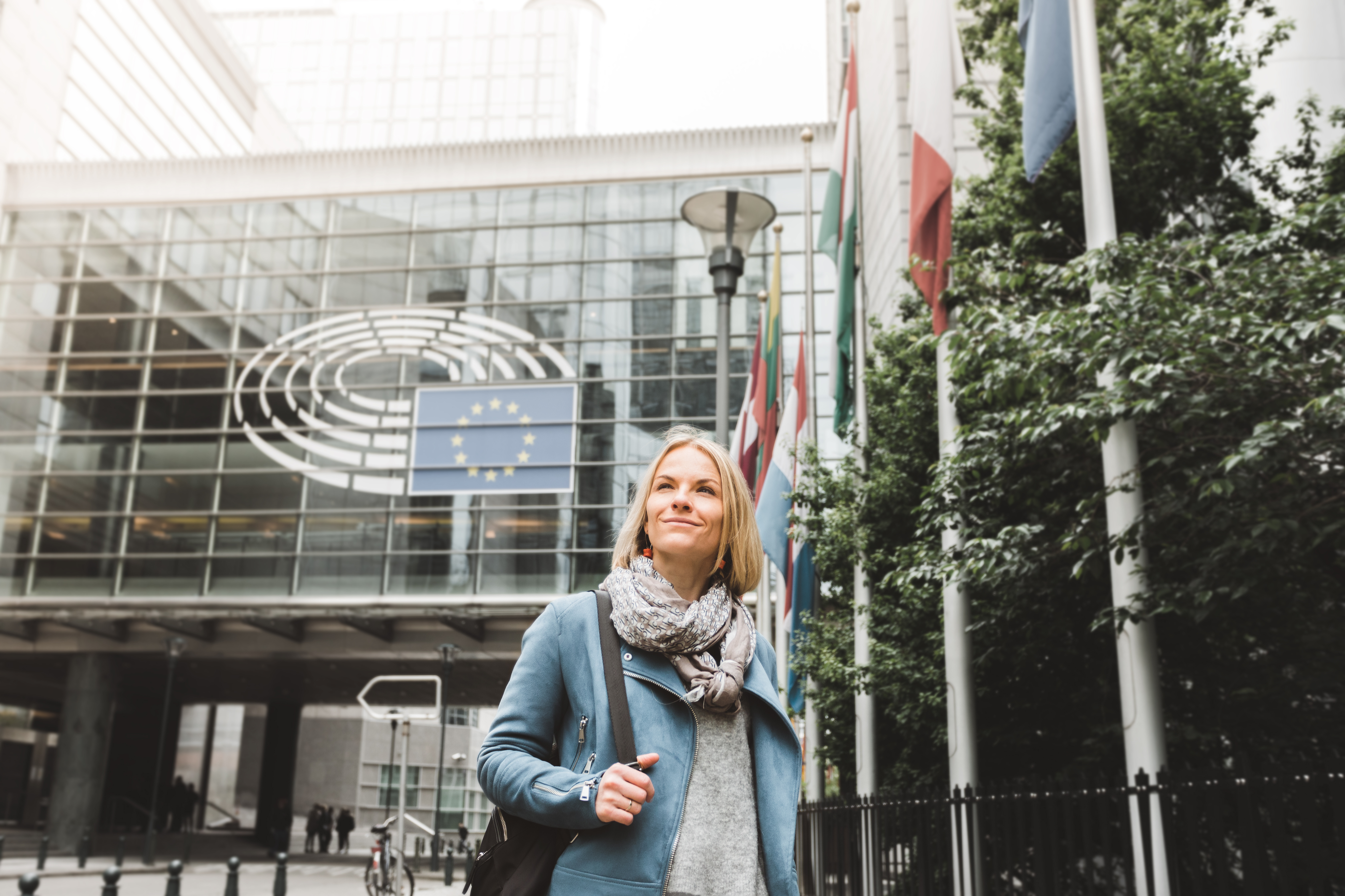 Kobieta stojąca przed budynkiem, na budynku znajduje się flaga Unii Europejskiej